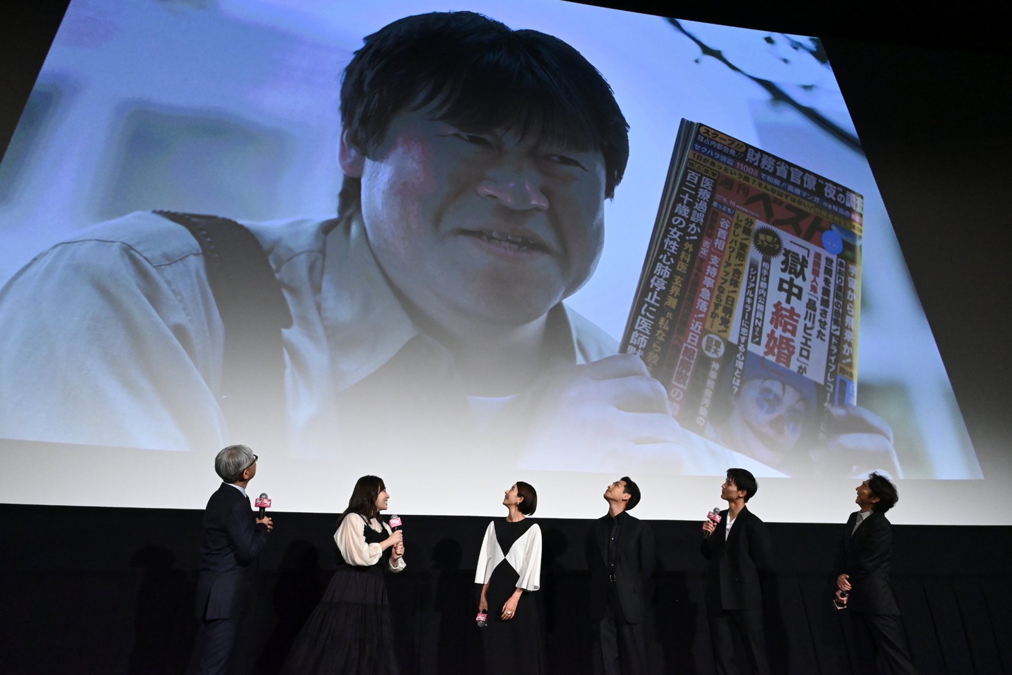 スクリーンに映し出された佐藤二朗を見上げる登壇者たち。