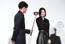 水上恒司（手前）が手にしたカメラにポーズを決める三吉彩花（奥）