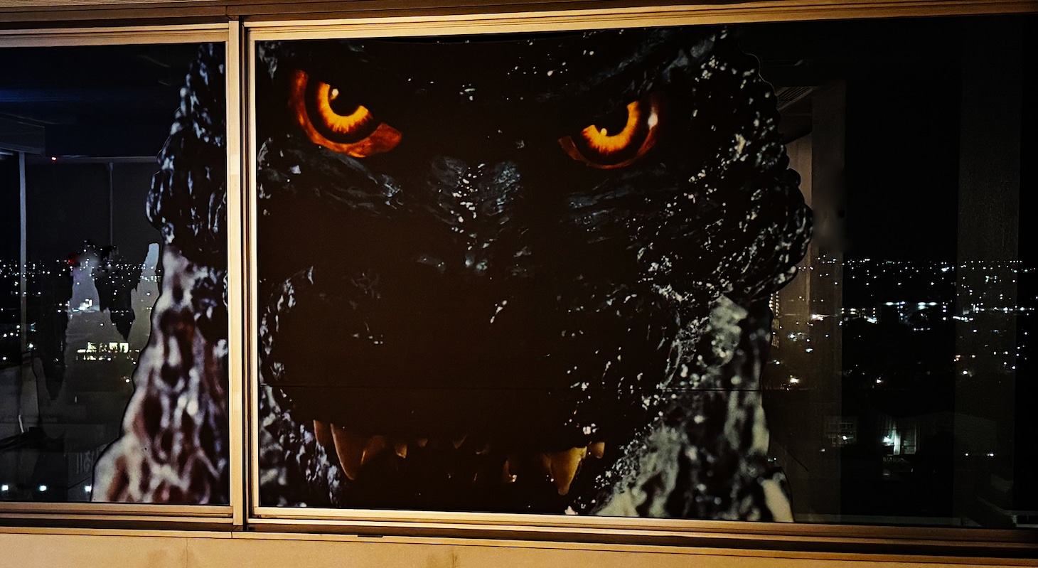 佐賀県庁の窓の外から建物の中をのぞくゴジラ（夜）