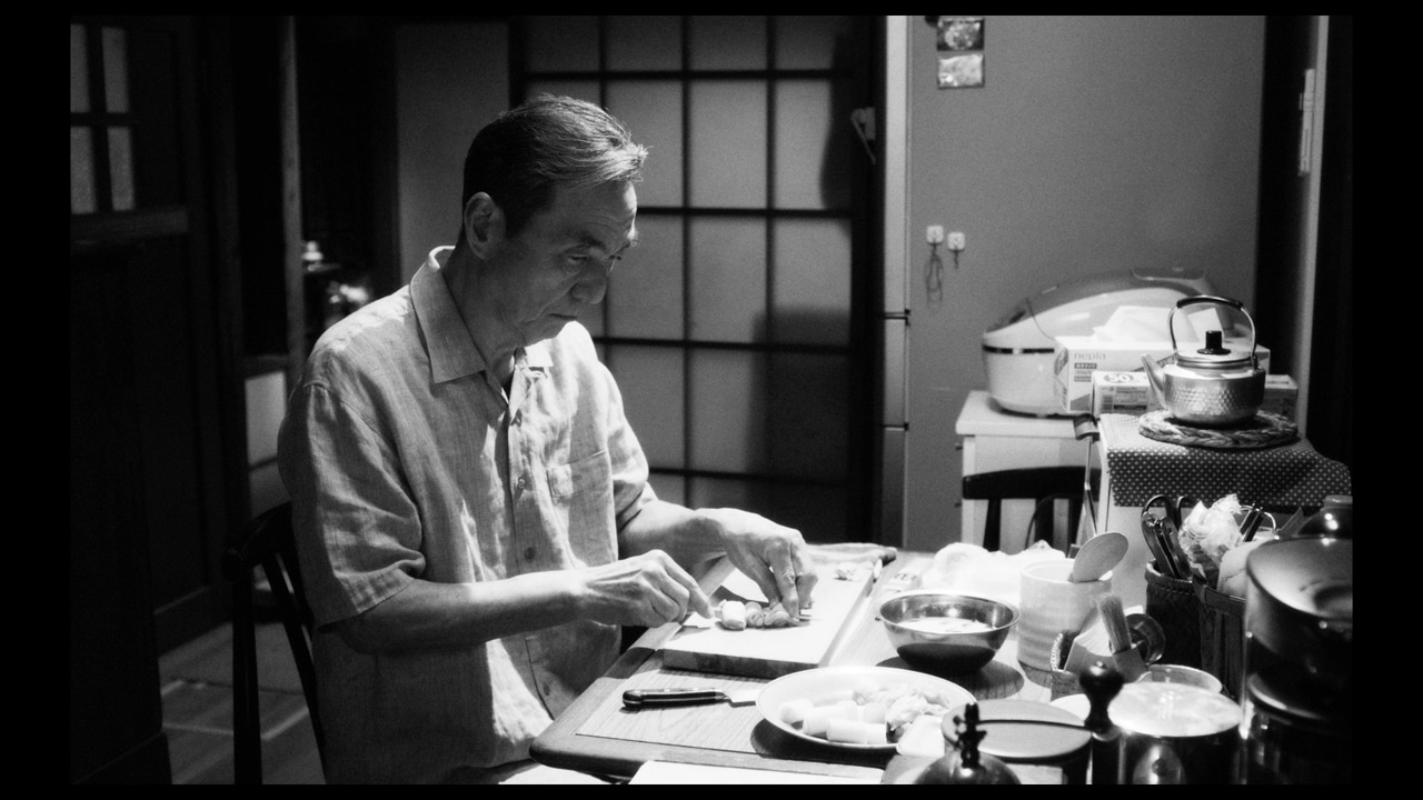 映画「敵」より、長塚京三演じる渡辺儀助が焼き鳥に串を打つ様子。