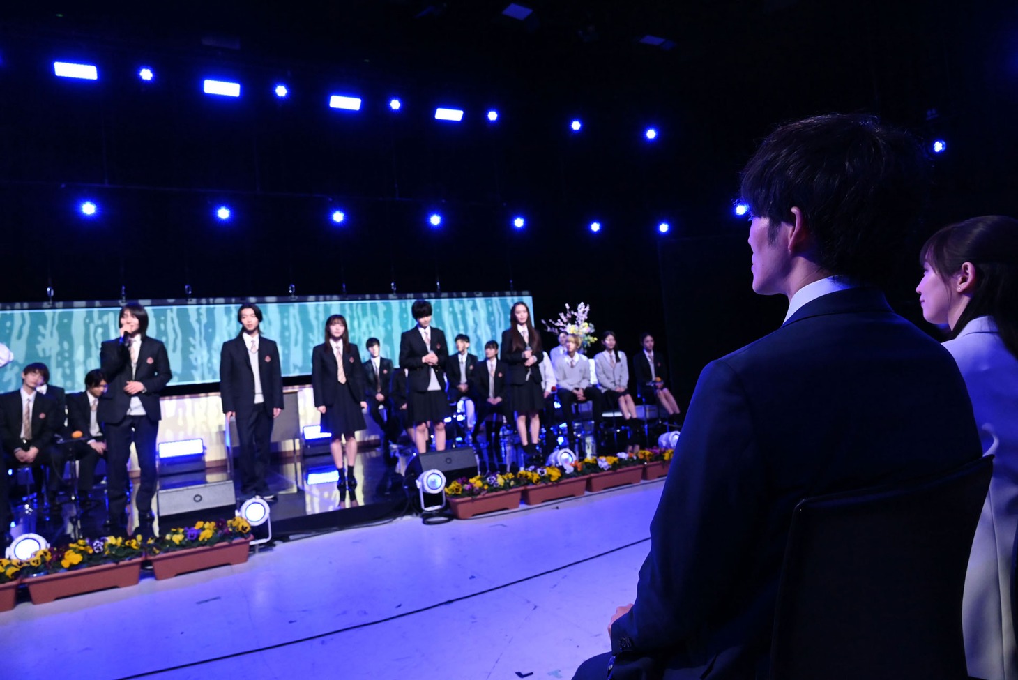 松坂桃李と吉岡里帆が、生徒たちの歌唱を見つめる様子