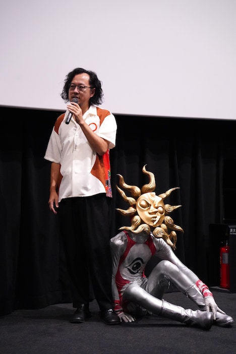 藤井亮(左)の足元に座り込むタローマン(右)