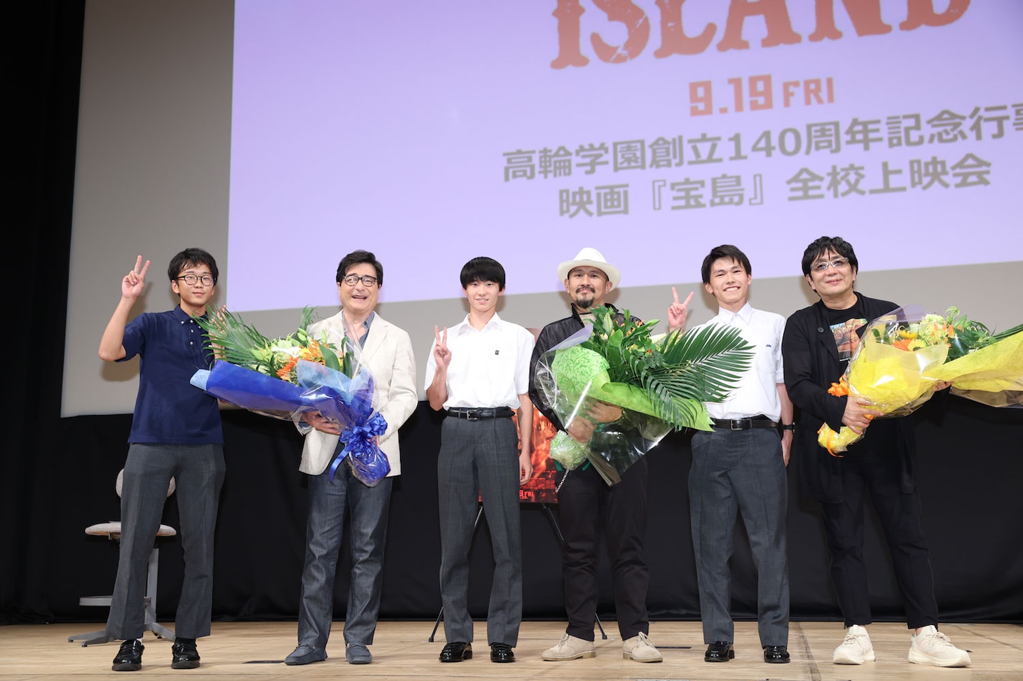 「宝島」特別上映会にて、学生たちと記念撮影するジョン・カビラ（左から2番目）、真藤順丈（中央）、大友啓史（右から2番目）