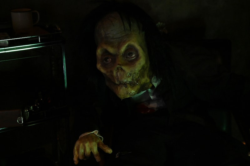 「ホラーにふれる展 －映画美術の世界－」に設置された「空室に住み着いた男」コーナー。“座ったまま事切れた男”が展示されている