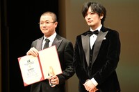 第10回ゴールドクレイン賞（金鶴賞）授賞式の様子。左からシャオ・ヤン（肖央）とプレゼンターの久保田悠来