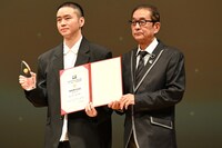 第10回ゴールドクレイン賞（金鶴賞）授賞式の様子。左からジャッキー・ガン（甘剣宇）とプレゼンターの滝田洋二郎