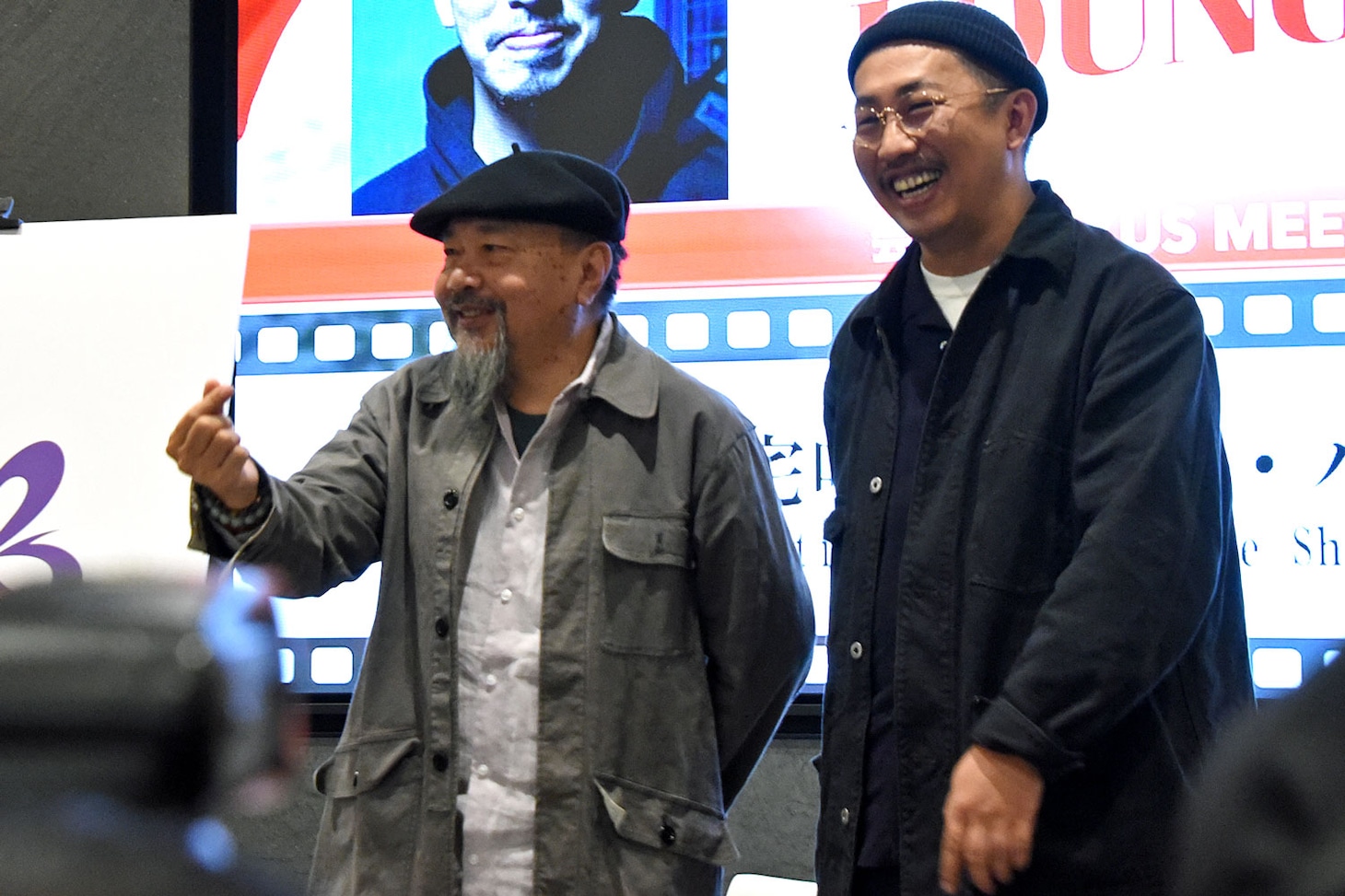 指ハートをカメラに向けるリティ・パン（左）と、笑顔を見せる三宅唱（右）