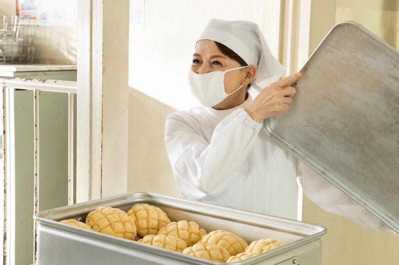 「おいしい給食 炎の修学旅行」場面写真。いとうまい子演じる牧野文枝がメロンパンを見せる様子