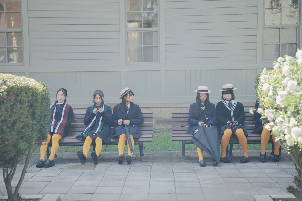 映画「白の花実」場面写真。カラータイツが目を引くコーディネート