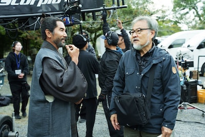 映画「黒牢城」撮影現場にて、談笑する荒木村重役の本木雅弘（左）、監督の黒沢清（右）