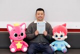 映画「ベベフィン・ザ・ムービー：うたとまほうのピンキッツワールド」ピンキッツ（左）とフィン（右）のぬいぐるみに囲まれたゲスト声優・ケンドーコバヤシ