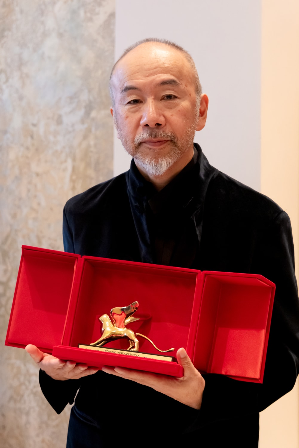 第83回ヴェネチア国際映画祭で、レオンチーノ・ドーロ賞のトロフィーを受け取った塚本晋也。黒いジャケット姿で、赤いベルベットの箱に収められた金色の有翼の獅子像を両手で胸の前に掲げている