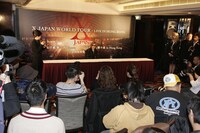 香港のメディアに囲まれるYOSHIKI。テーブルには水の入ったコップが置かれているが、YOSHIKIからは若干遠い。