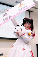 レーベルロゴ（左）が描かれたパネルを掲げるモモーイ。アニメ美少女の目をモチーフにしたロゴはモモーイ発案によるもの。