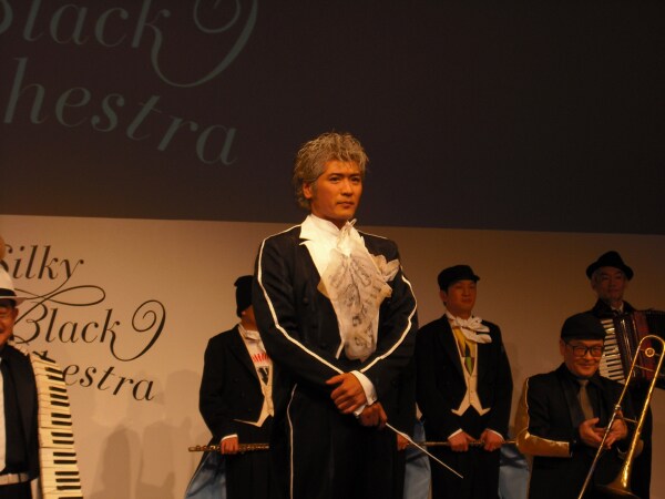 真剣な面持ちでじっと正面を見据える吉川晃司（写真中央）と、トロンボーンを手に意味深な笑みを浮かべる仲本工事（写真右端手前）。奥にはスチャダラパーの姿も。