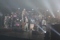 お揃いのつなぎを着込んで演奏するユニコーンの5人。この日の衣装は、ツアー中に一番多く着用したアーミーグリーンのつなぎ。背中にはメンバーを表すアルファベット1文字が入っている。ちなみに武道館3DAYSの初日となった5月19日には赤のつなぎ、2日目の5月20日にはジャケットとネクタイの学生コスプレで登場した。