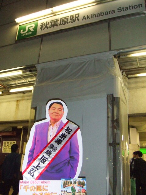 世界最大の萌えシティ、秋葉原の駅前に佇む坂上弘の等身大パネル。おじいちゃん萌えの若者に持ち去られてしまわないか心配だ。