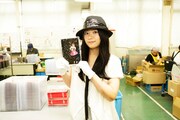 できたてのアルバムを手にしてよろこびの笑顔を浮かべるアイラと、黙々と作業を続ける工員。