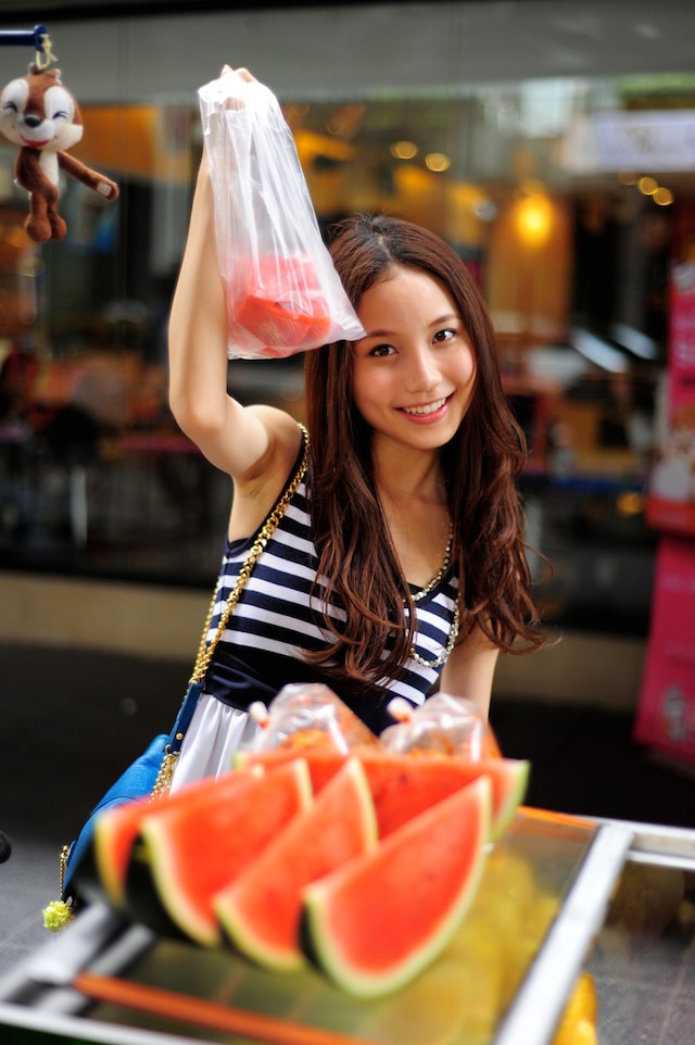 歌声でタイと日本に友好の橋を架けるMay。スイカの入ったビニール袋を持ってニッコリ。