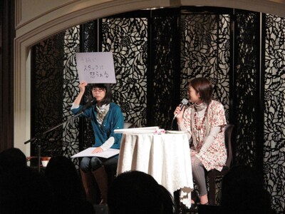 頭上にフリップを掲げて知られざるエピソードを次々と話すつじあやの（写真左）。