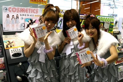 タワーレコード渋谷店2FのJ-POPフロアで展開されているCOSMETICSコーナーの前で、CD「LOVE IS ALL」を持って記念撮影をするCOSMETICSの3人。