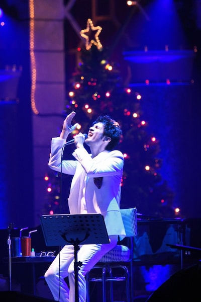 巨大なクリスマスツリーをバックに熱唱する平井。白いスーツがお似合いだ。