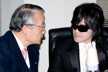 河合弁護士（写真左）は、「私のところに来たときは本当に声が出なくて、何度も聞き返さないと聞こえないほど、弱々しく振り絞る感じ。歌手としての生命がこのまま終わってしまうんじゃないかと思った。驚いたのは、ロスから帰ってきたら（TOSHIの）顔色や表情が以前とは違い、声の様子も違ったので、環境の変化が精神的なものに影響したのかと思った。とてもじゃないが仮病とは思えないし、大変驚いている」とTOSHIの変化について語った。