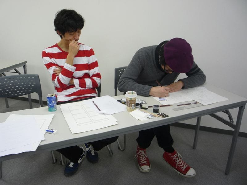 楳図かずおチックな赤いボーダーシャツを着こなすズィ～レイ（写真左）、マンガの神様を思わせるベレー帽姿で執筆に励むJxJx（写真右）。