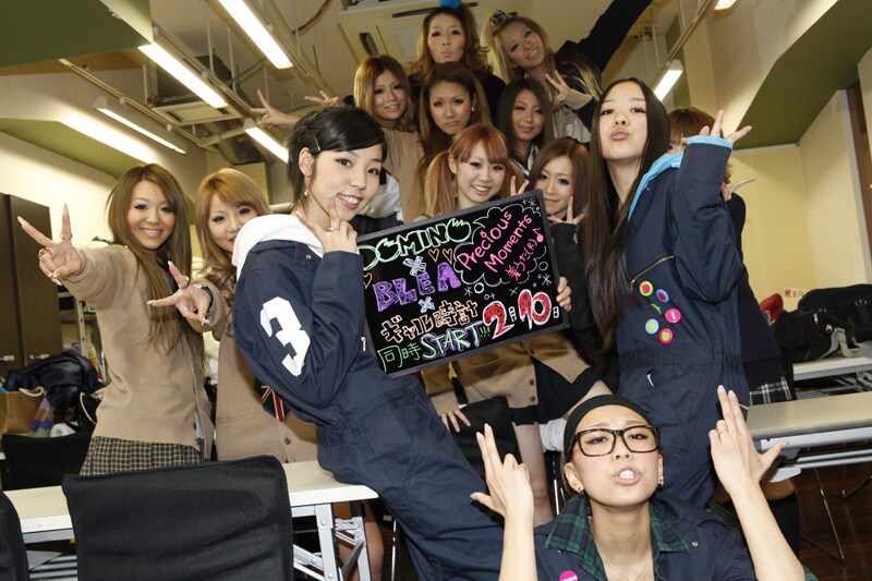 教室で「GAL-tokei（ギャル時計）」のための写真撮影をするDOMINOの3人と女子生徒たち。