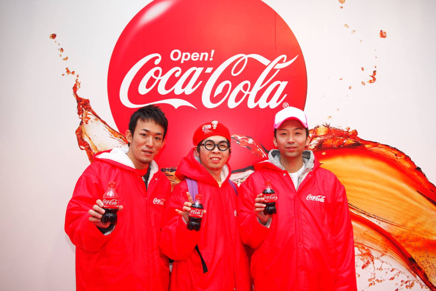 背景、ベンチコート、現物とコカ・コーラ一色の中でポーズするFUNKY MONKEY BABYS。