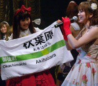 オタクカルチャーの発信地、秋葉原を象徴するJR表示板を模したノボリを掲げるモモーイ。