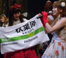 オタクカルチャーの発信地、秋葉原を象徴するJR表示板を模したノボリを掲げるモモーイ。