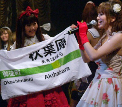 オタクカルチャーの発信地、秋葉原を象徴するJR表示板を模したノボリを掲げるモモーイ。