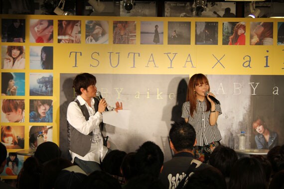 MCの荘口彰久と爆笑トークを繰り広げるaiko。この日のファッションは、黒いギンガムチェックのシャツにスカートという春らしい装い。