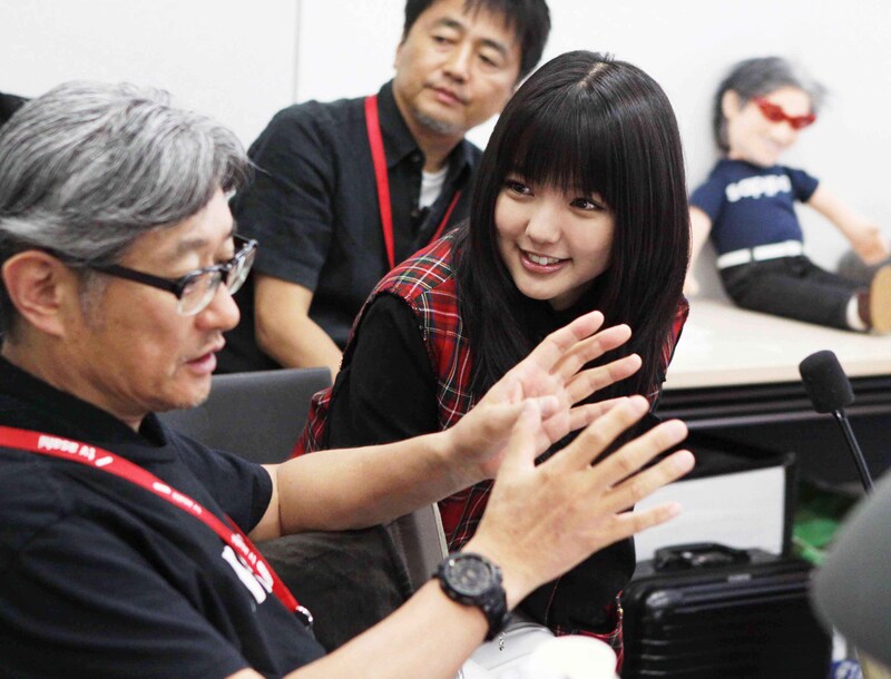 映像の意図を説明する堤幸彦と、監督を笑顔で見つめる真野恵里菜。