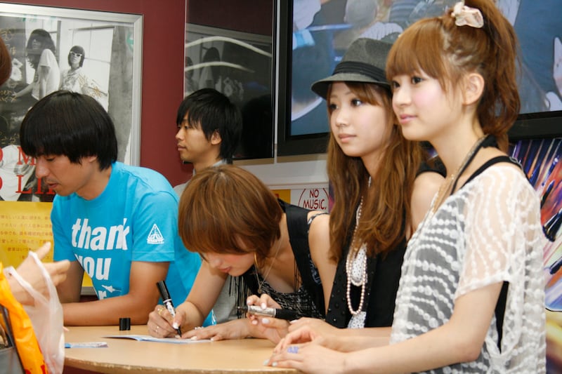 アルバム「thank you for the music!」のブックレットに、それぞれサインをするふかわりょうとCOSMETICS。