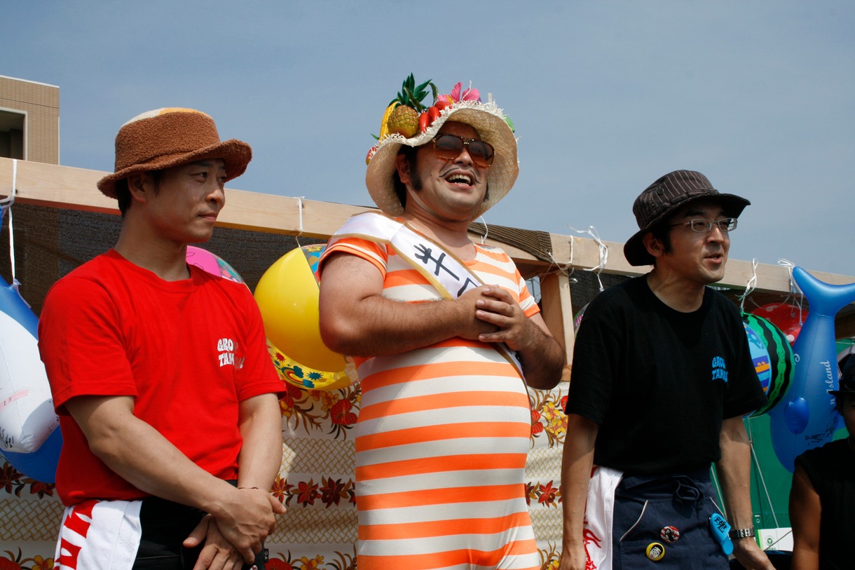 来場した観客を前に挨拶する港カヲル（写真中央）、バイト君（右）、石鹸（左）。バイト君と石鹸は店員のため前掛けを着用。