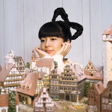 写真は1stシングル「オーロラに隠れて」ジャケット。メルヘンチックなミニチュアの街並を眺めてうっとりする南波志帆。