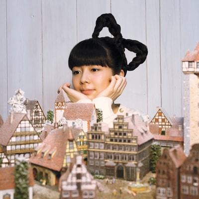 写真は1stシングル「オーロラに隠れて」ジャケット。メルヘンチックなミニチュアの街並を眺めてうっとりする南波志帆。