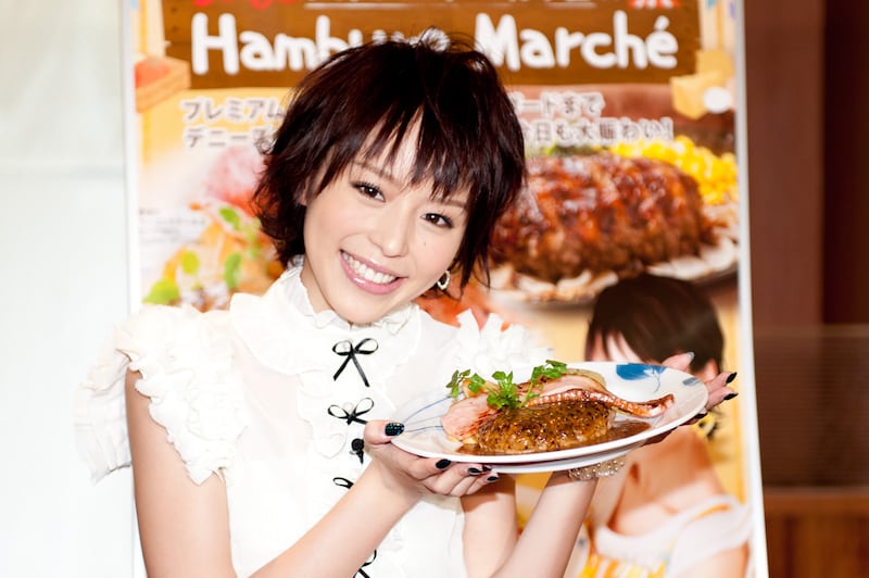 平野綾が手にしているのは「ハンバーグ マルシェ」イチ押しメニュー「厚切りベーコンステーキ＆ビーフ100%ハンバーグ」。