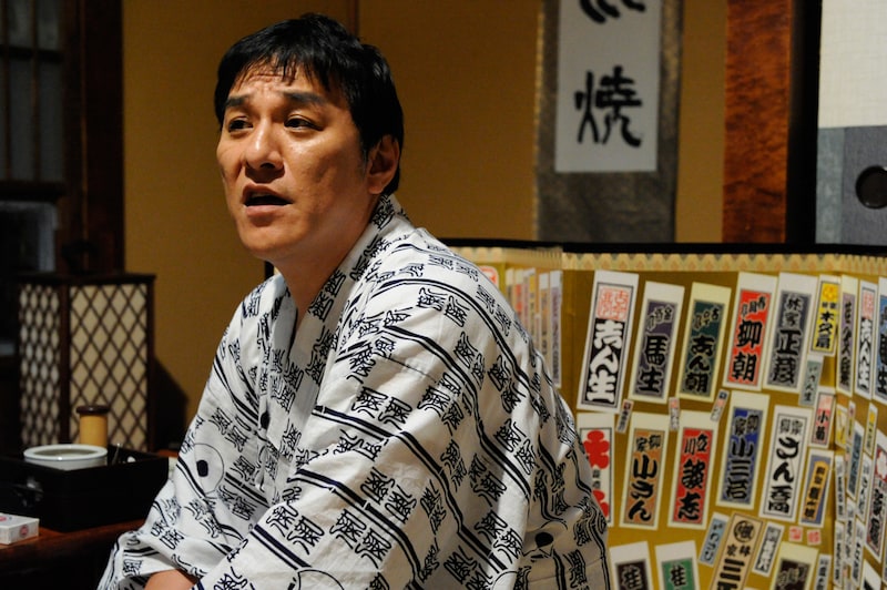 ピエール瀧扮する今戸家小六。瀧はしん平監督から「古典落語とは演者が工夫を加えて自分のレパートリーにしていくもの」と教えてもらい、「ひとつ足すことで小六になりきれる」と解釈。多くのシーンでアドリブを連発し、そのセンスを監督に絶賛された。ちなみに劇中で演じる古典落語の演目は「強情灸」。（C）2011「落語物語」製作委員会