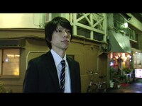 映画「シンクロニシティ」のワンシーン。富澤タク演じるスーツ姿の男。