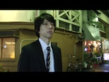 映画「シンクロニシティ」のワンシーン。富澤タク演じるスーツ姿の男。