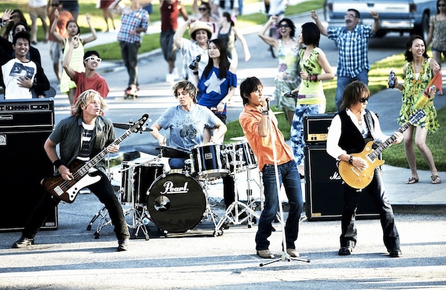 広大な住宅街セットの中で熱演するB'z。バックを務めるのは彼らのライブではおなじみのシェーン・ガラス（Dr）とバリー・スパークス（B）の2人。