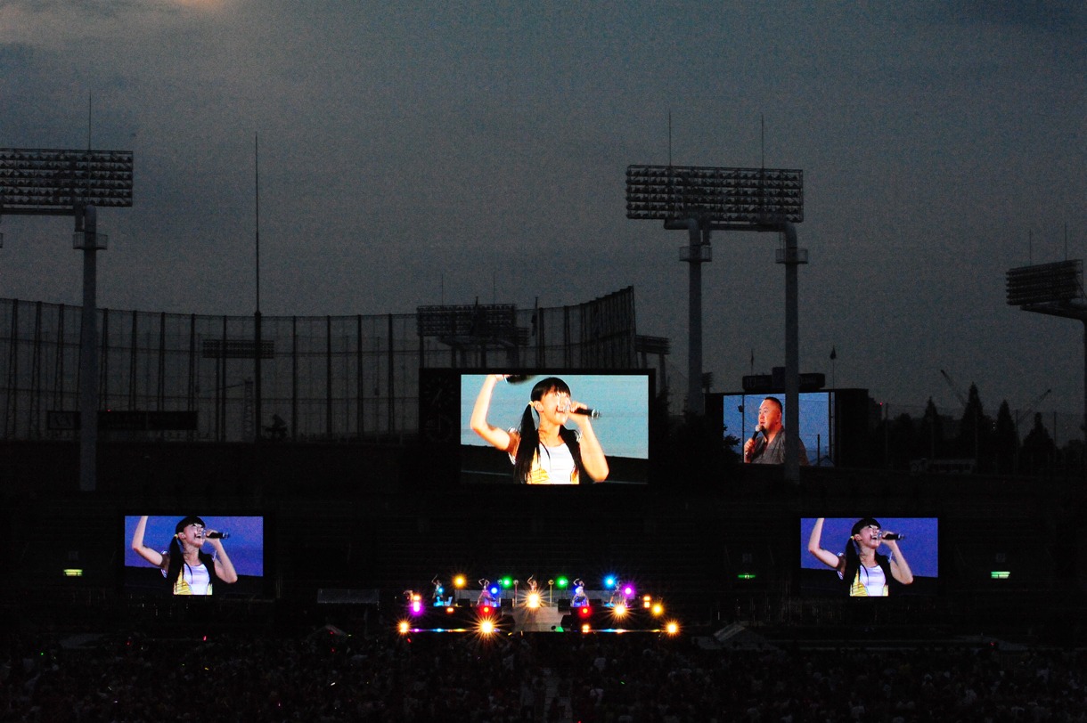 写真は8月6日の「神宮外苑花火大会」より。夕闇に浮かぶ玉井詩織と神宮球場の松村邦洋。