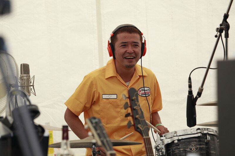 ドラムを叩く奥田民生。黄色い「カンタビレ」ワークシャツがお似合い。