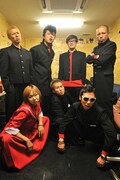 楽屋で記念撮影するヒダカトオルバンドと吉村秀樹。楽屋には綾小路翔から「ステージでは手を抜いて頂けますと大変助かります」という手紙を添えて、1個630円のマンゴープリンが差し入れされた(撮影:小川舞)。