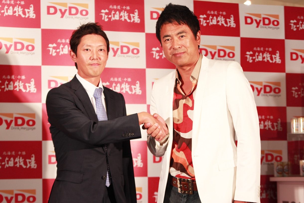固い握手を交わすダイドードリンコの営業本部長・高松富也氏（写真左）と田中義剛（右）。ちなみに高松氏と庄司智春は同じ35歳で、ダイドードリンコは今年で創業35周年。そして義剛が牧場経営を始めたのも35歳の頃、と3者には意外な共通項が。