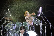ドラムを叩きながら激しく水をまき散らすYOSHIKI。手前はToshI。