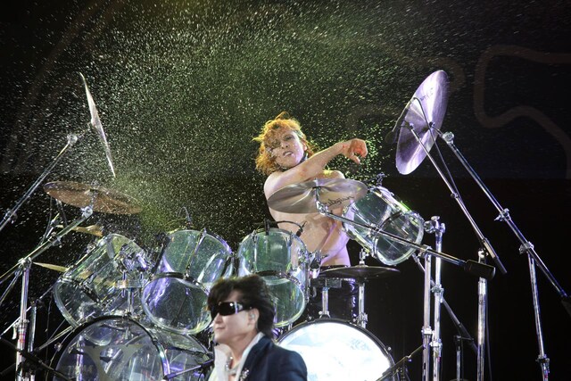 ドラムを叩きながら激しく水をまき散らすYOSHIKI。手前はToshI。